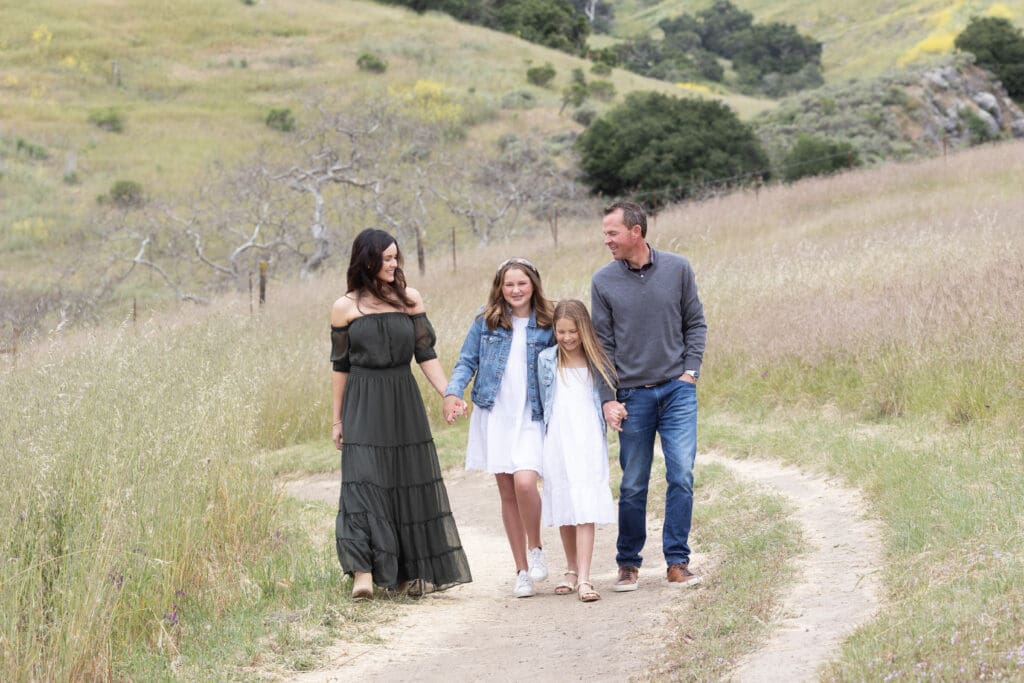 a mom and dad walking down a dirt path with their two daughters