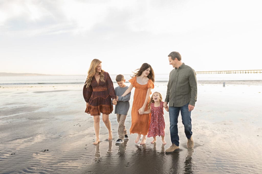 best-locations-for-family-photos a family of five walking down the beach with the pier in the background during the best locations for family photos
