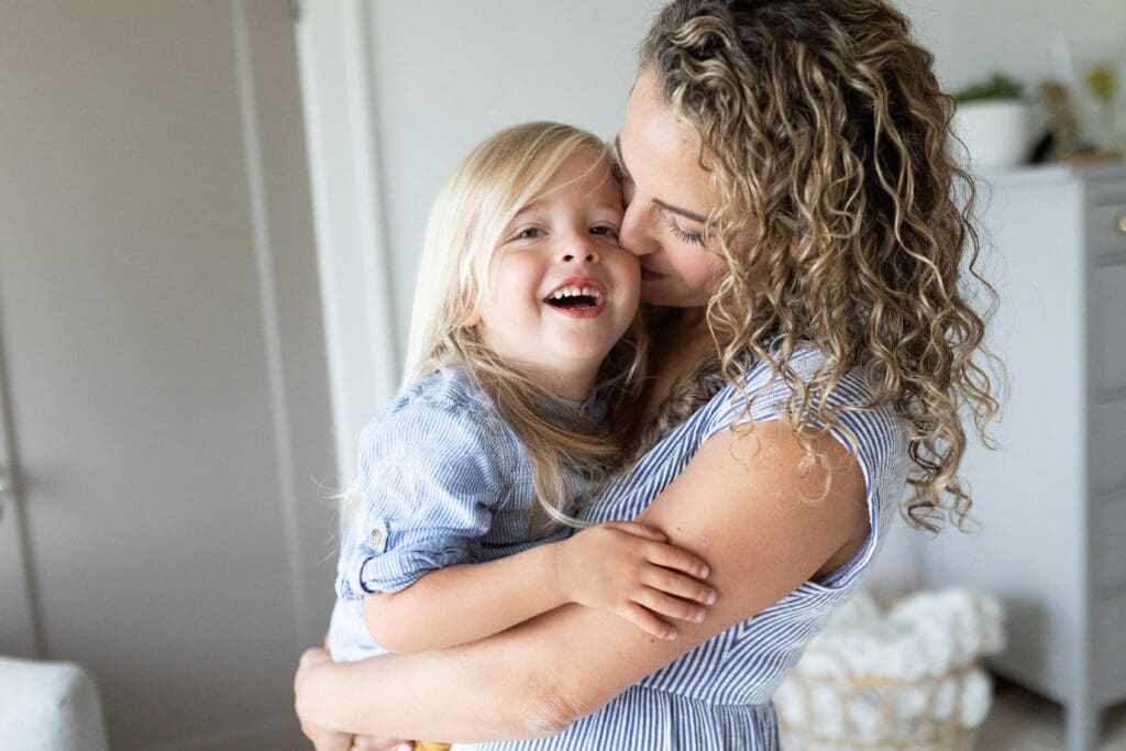 Mother holding her young daughter close and smiling at home, showing the warmth and connection families look for when choosing the right photographer.