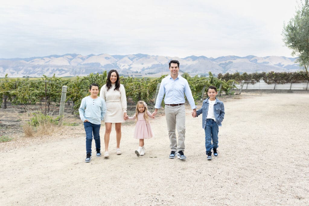 Family walking hand-in-hand through a vineyard with mountains in the background, showing the relaxed connection that comes from choosing the right photographer.