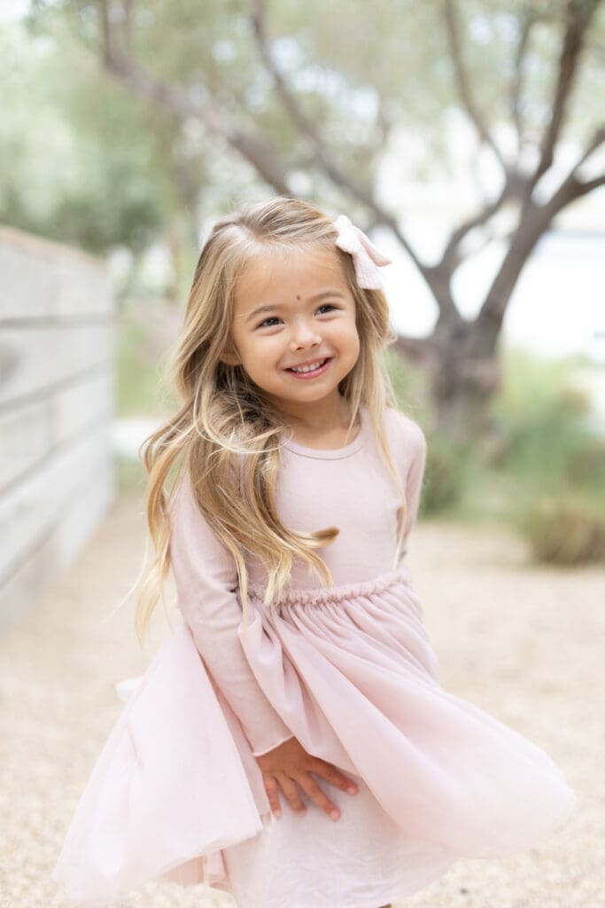 Young girl in a pink dress smiling softly outdoors, showing the natural beauty and warmth that comes from choosing the right photographer.