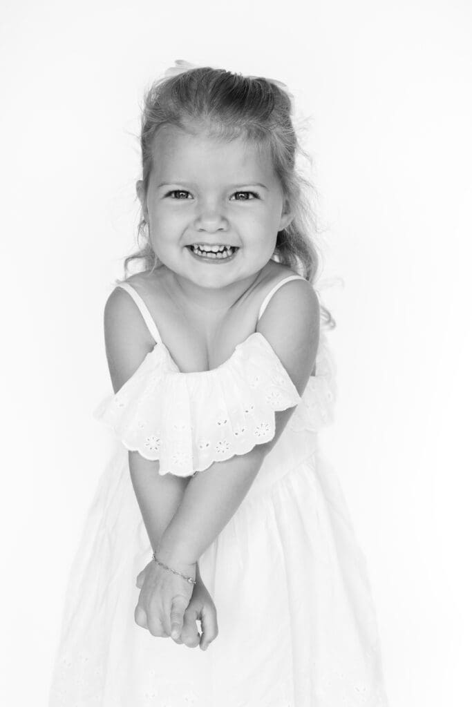 Smiling young girl in white dress, captured in a bright, joyful moment for family photos at home.