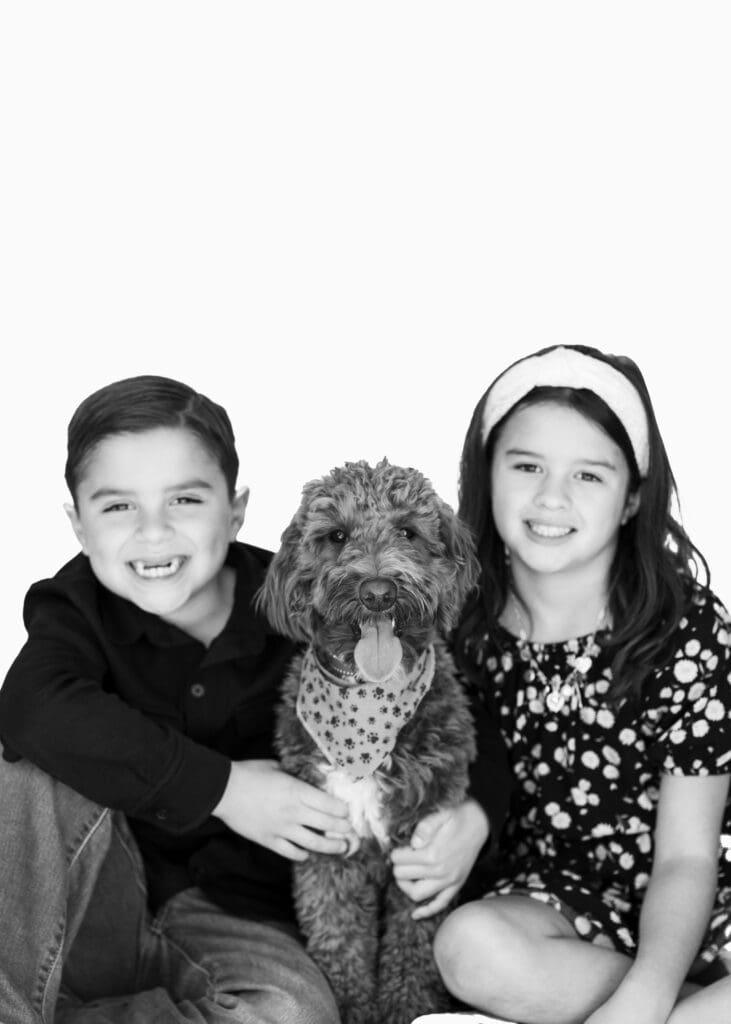 Smiling siblings with their dog in a joyful black and white portrait, perfect for family photos at home.