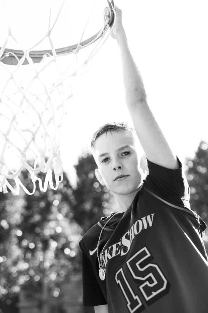 Confident boy in basketball jersey by hoop, capturing personality and passion in family photos at home.