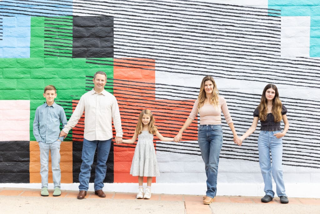 Family of five holding hands and standing in front of a colorful mural during a professional family photography session in San Luis Obispo.