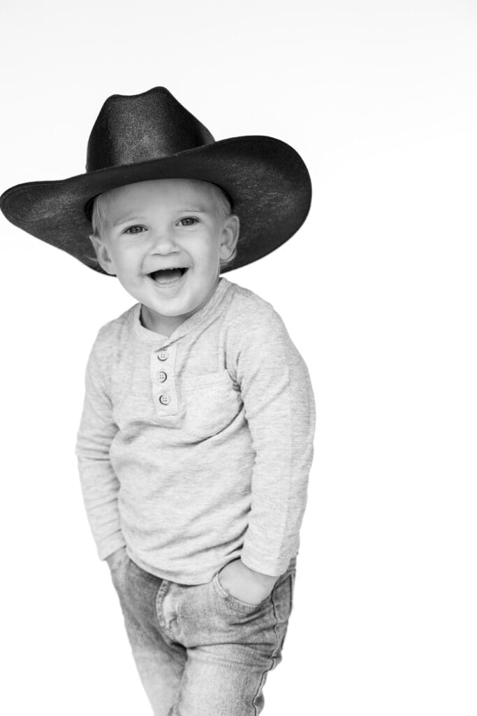 Smiling toddler in cowboy hat during a  photo session in studio, black and white portrait.