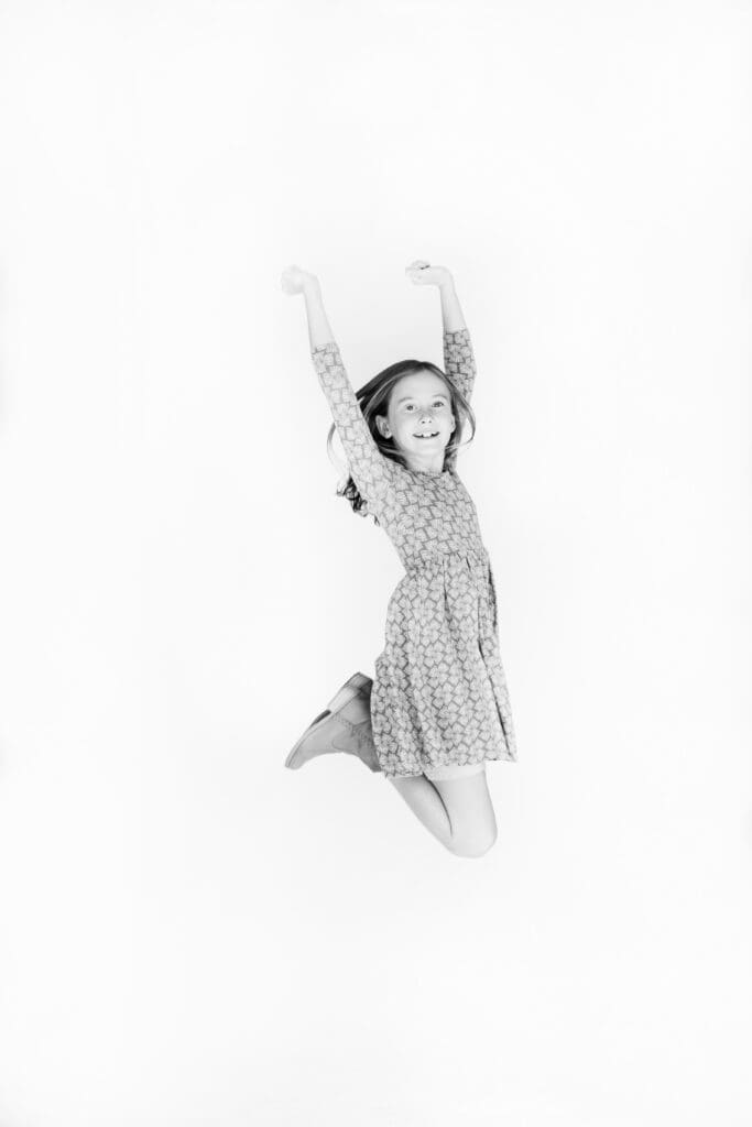 Young girl mid-jump with joyful expression during a candid kids photo session in studio, black and white image.