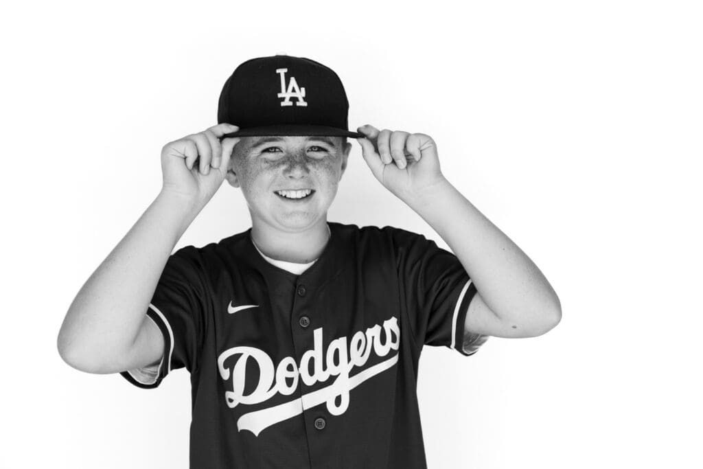 Smiling boy in Dodgers jersey adjusting cap 