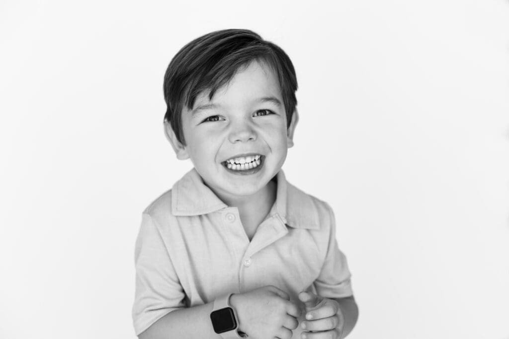 Happy young boy in collared shirt smiling brightly during preschool photos against a simple white background.