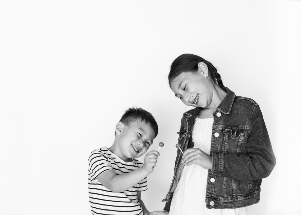 A boy and girl laugh joyfully while holding lollipops, sharing a carefree, happy moment.
