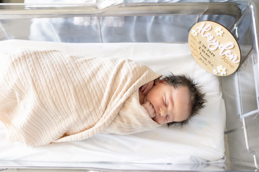 Newborn baby wrapped in a cream swaddle during Fresh 48 photos at the hospital bassinet.