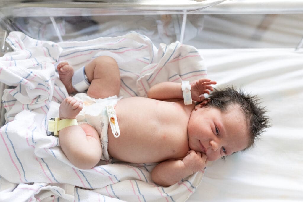 Newborn baby lying on hospital blanket with diaper and wristbands, captured during first day of life.