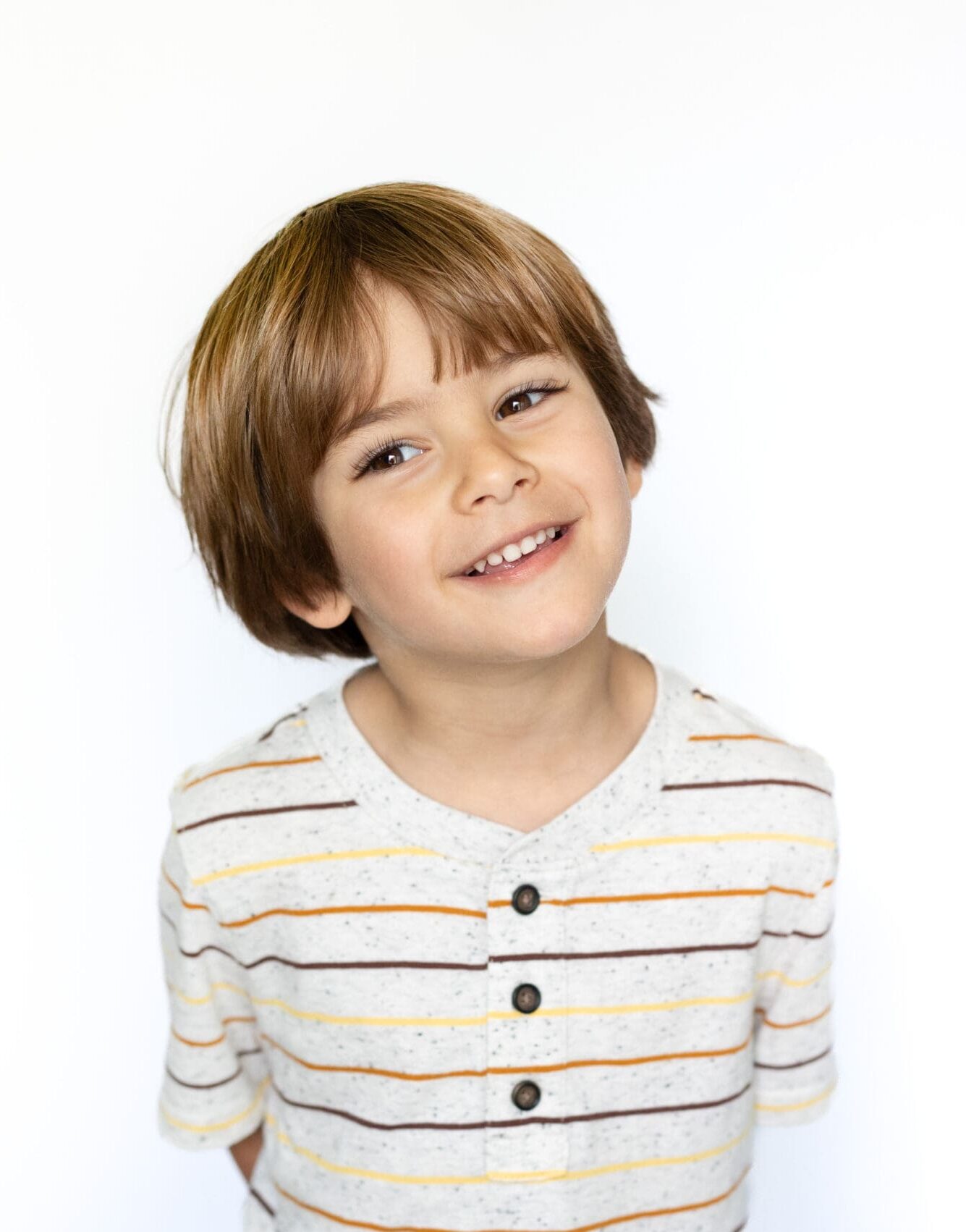 Cheerful young boy in a striped shirt, tilting his head slightly with a bright smile.