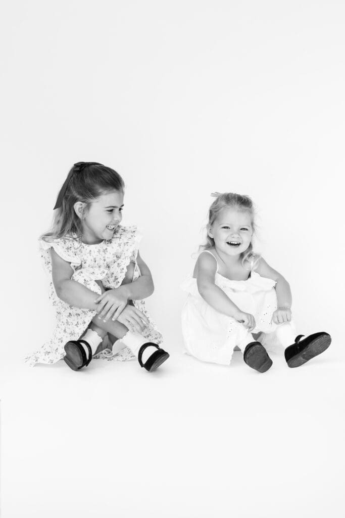 Two young sisters laughing in a bright studio setting, a sweet example for questions to ask a photographer before you book.