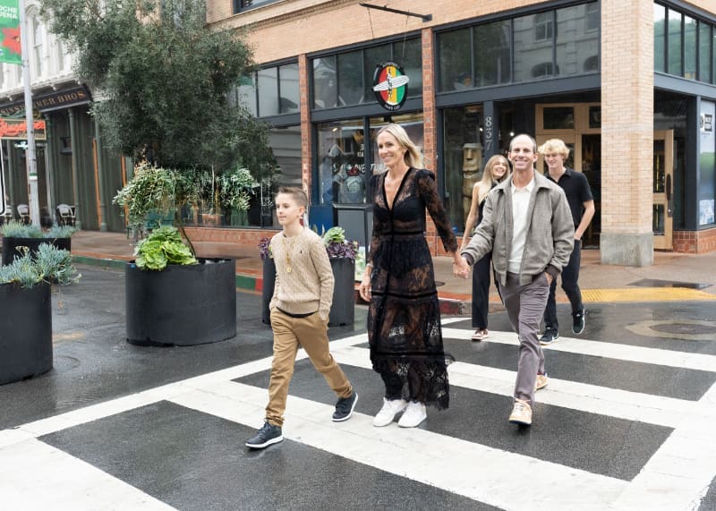 Family walking across a crosswalk downtown, sharing candid family moments full of connection and movement.