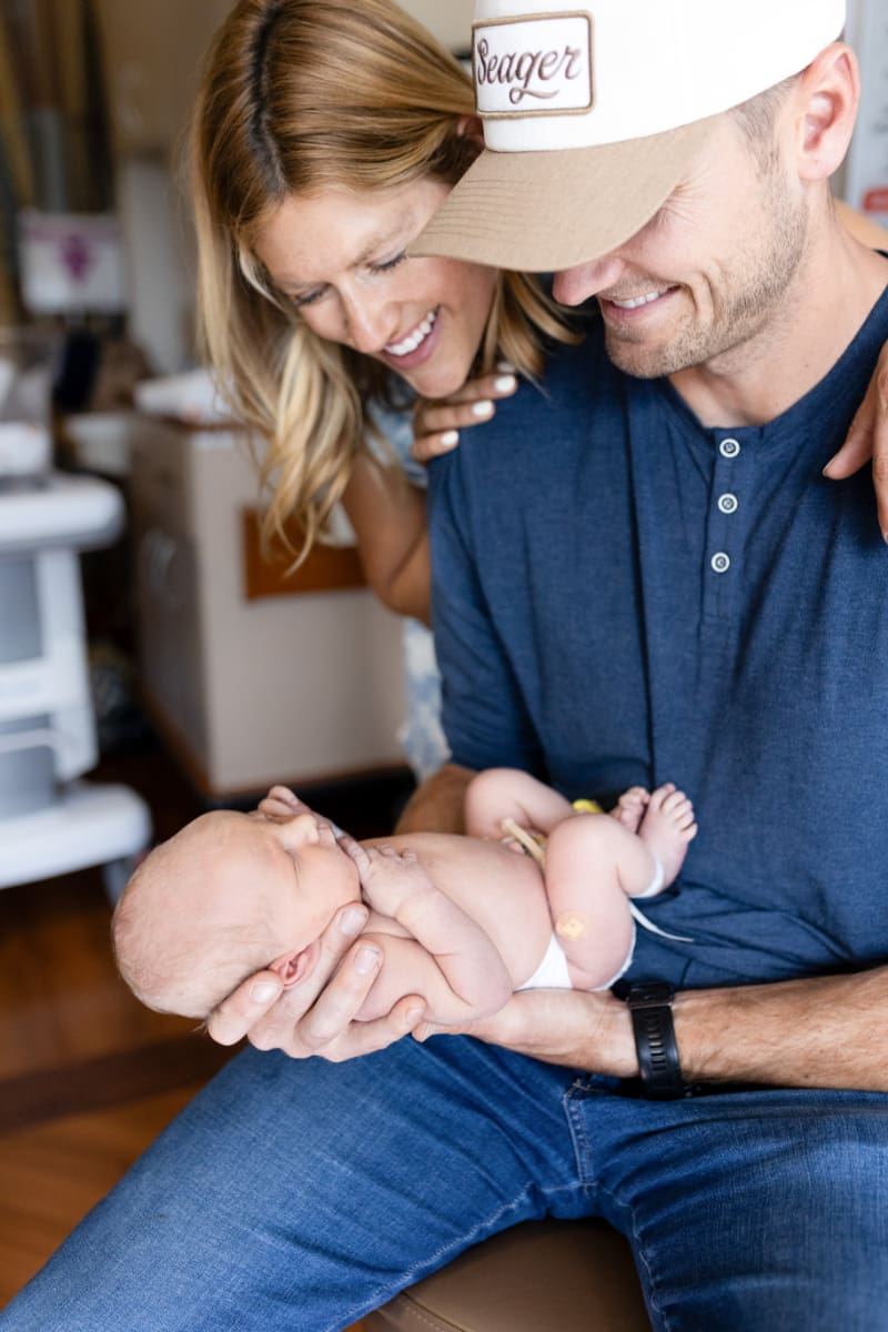 New parents smiling at newborn in hospital, showing how to feel confident in front of the camera.