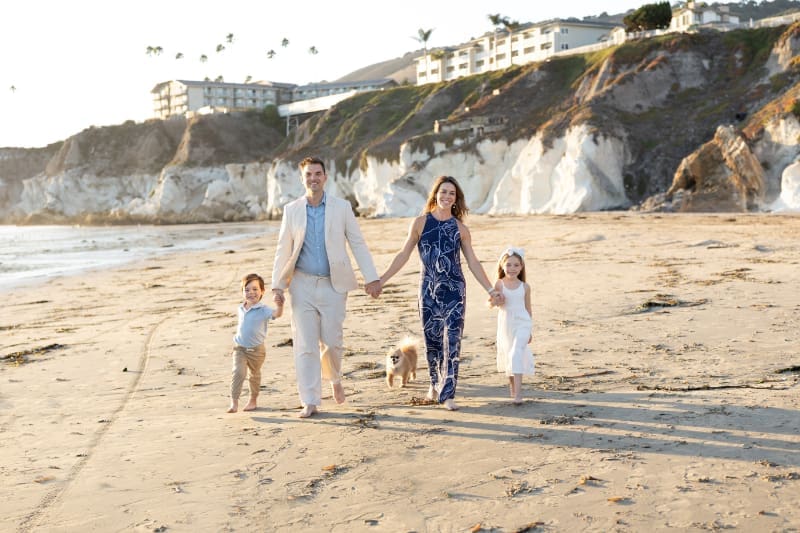Family walks barefoot on the beach at golden hour, enjoying the best time of year for family photos.