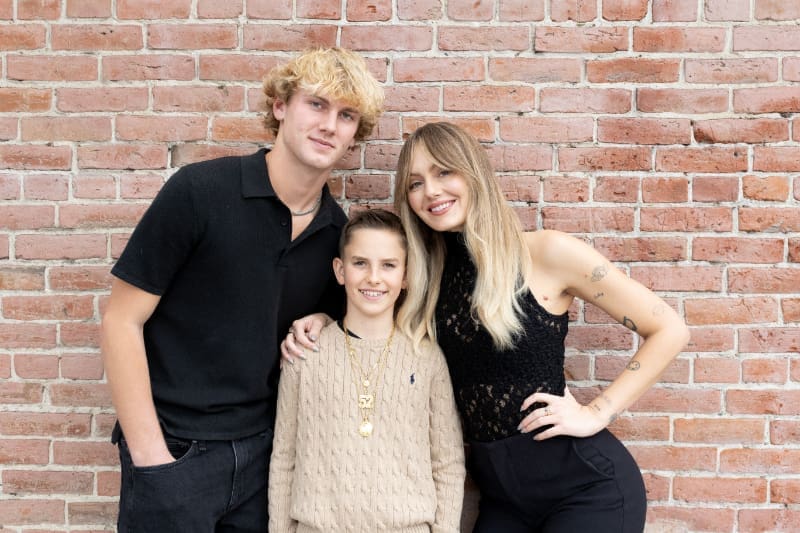 Siblings smiling together in front of a brick wall, showing style, connection, and strong family bonding.