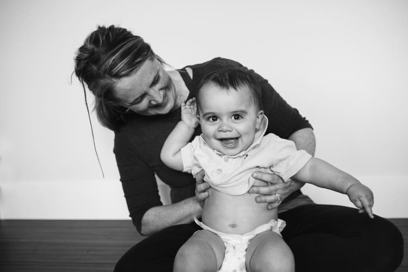 Smiling baby sitting on a woman’s lap, both sharing a playful, joyful moment together indoors.