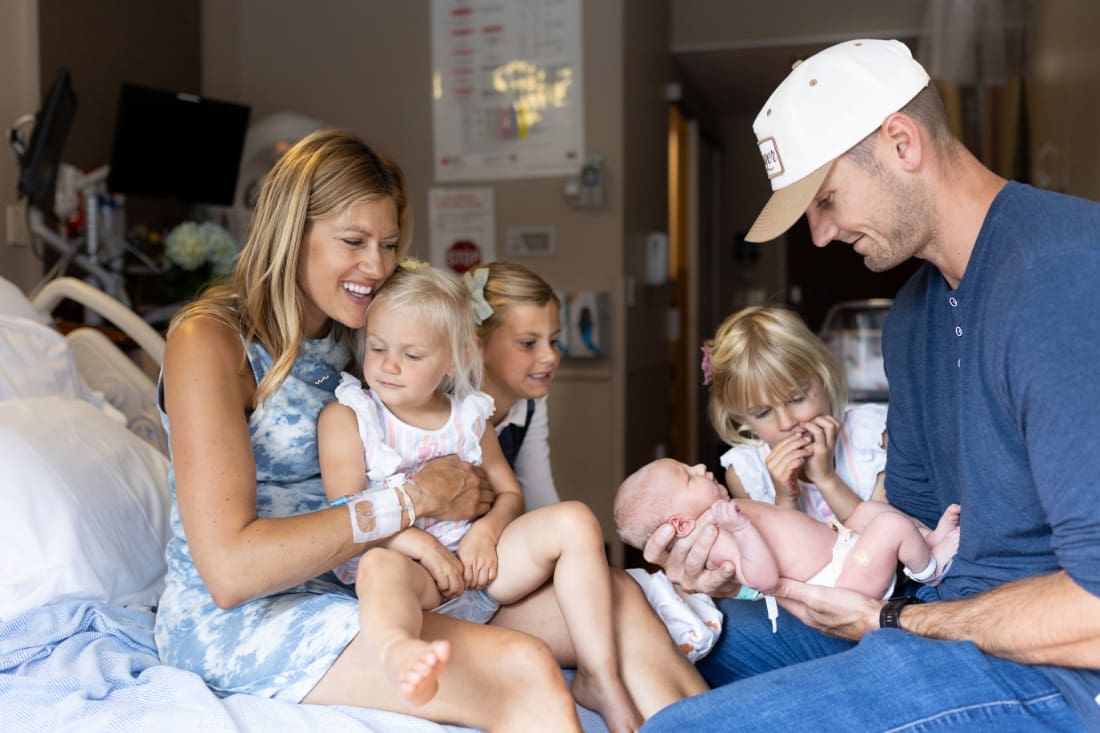 Lifestyle newborn family photos in hospital room with parents and siblings gathered around baby