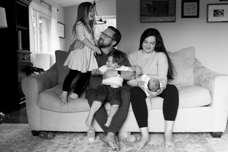 In-home newborn family photos of parents cuddling children on cozy couch.