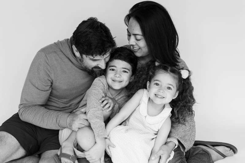 Black and white portrait of smiling family cuddling close together in studio.