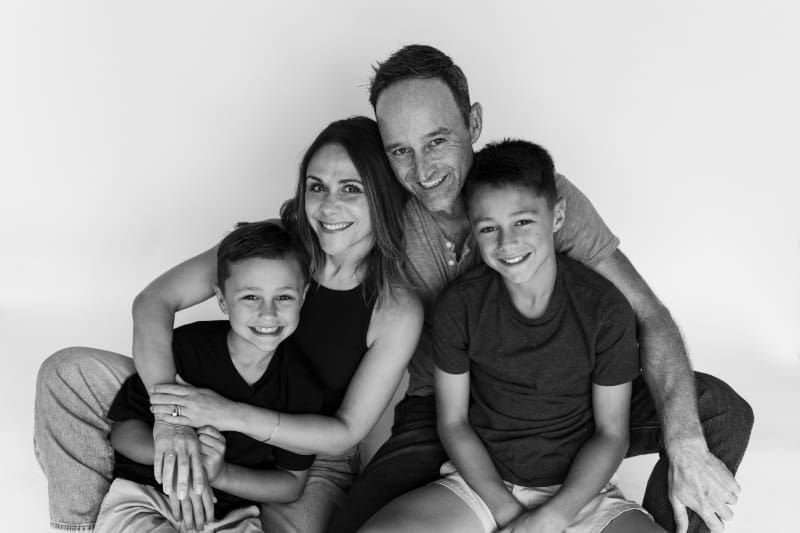 Timeless photography of smiling family portrait with parents and two sons embracing.