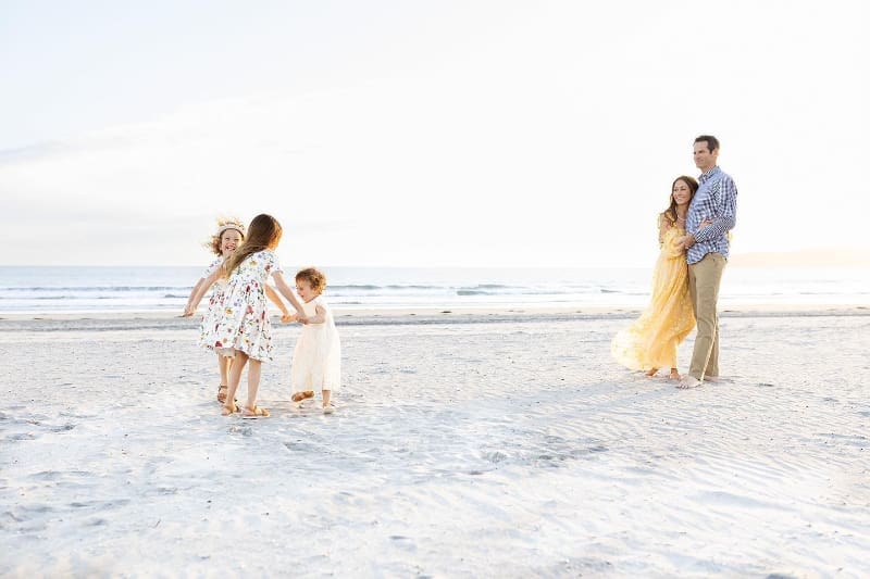 Photo of a family walking and playing together on soft beach at sunset.