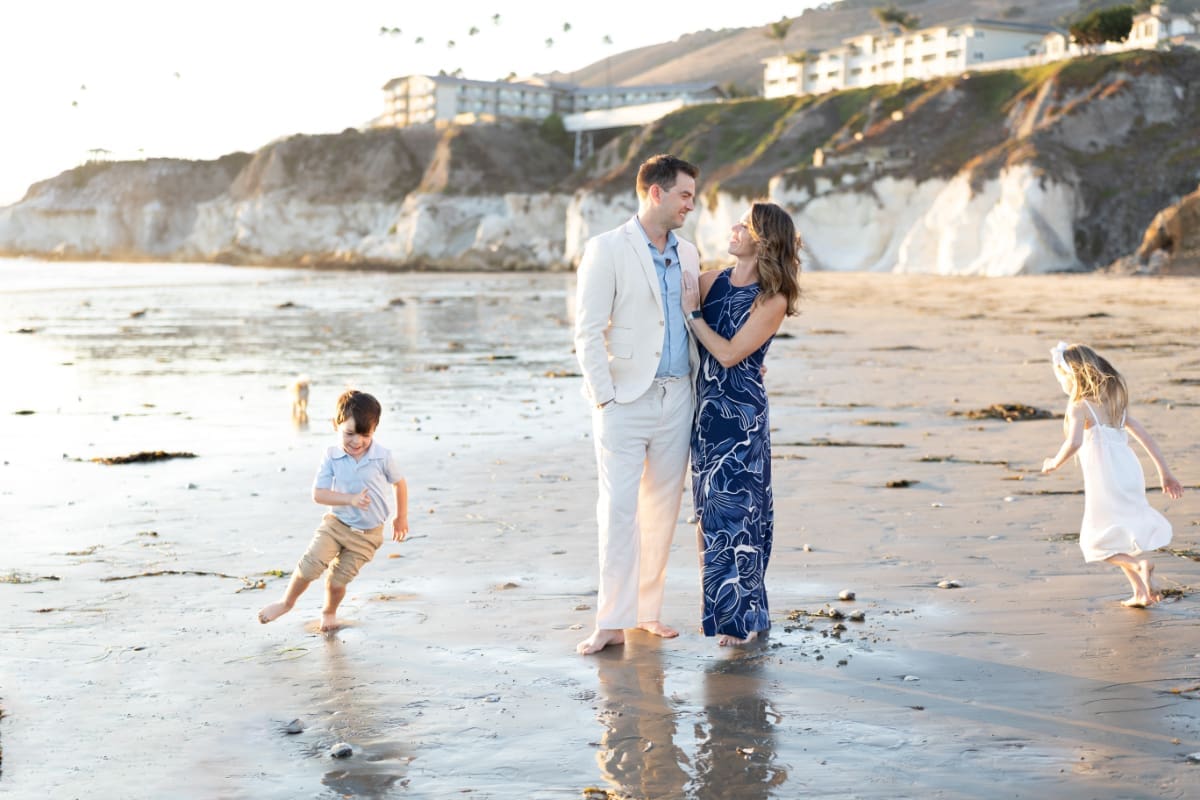 Family photos on the beach of parents smiling together while kids run and play along shoreline at sunset