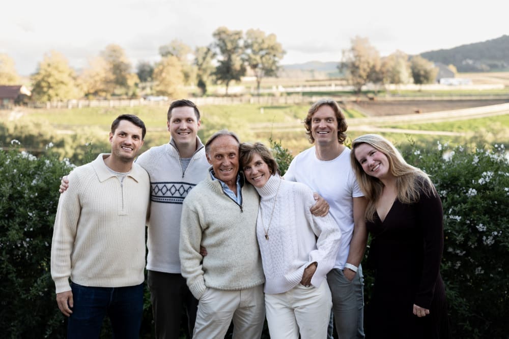 Extended family photos of adult siblings with parents outdoors, smiling together in soft natural countryside setting