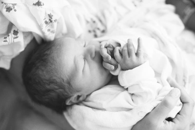 Lifestyle newborn photography of a sleeping newborn cradled in a parent's arms during an in-home session.