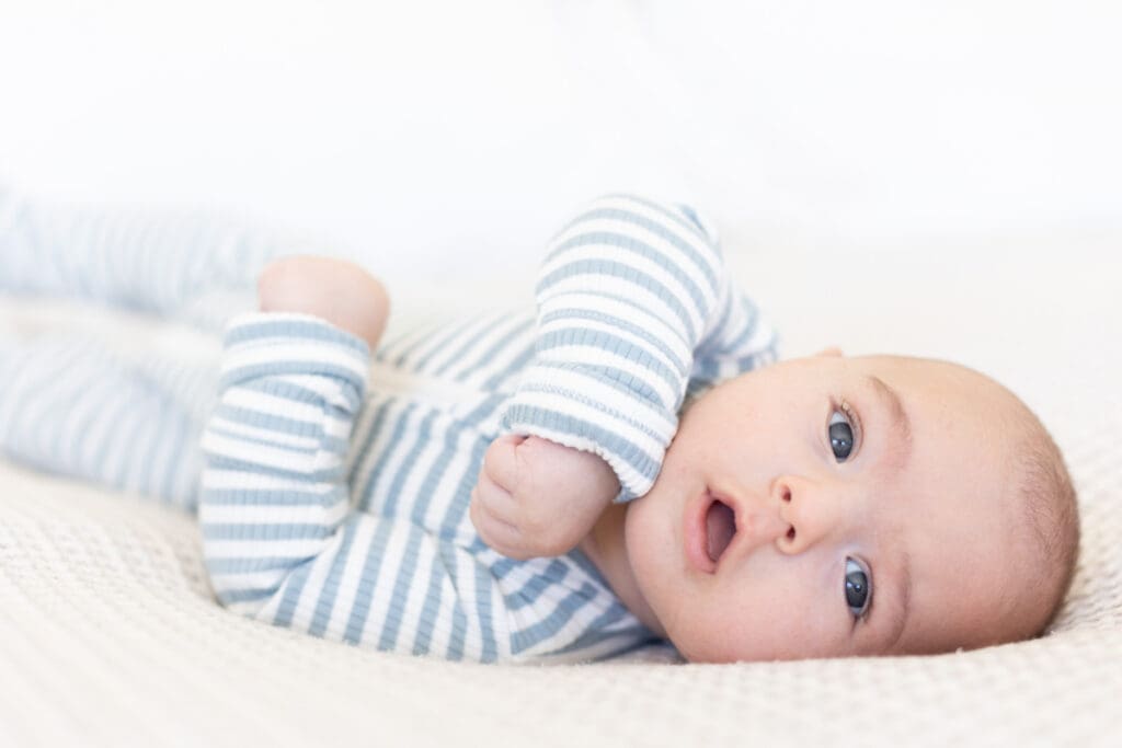 Lifestyle newborn photography of an awake baby in a striped sleeper, lying comfortably on a bed at home.