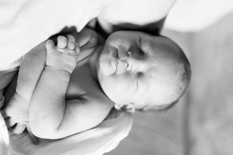 Newborn baby sleeping peacefully while being gently supported in a parent's hands.