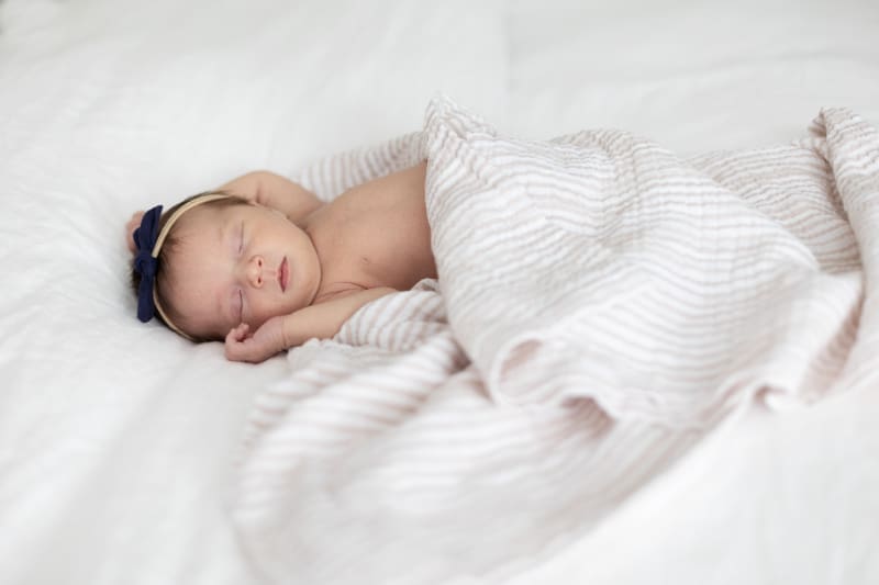 Lifestyle newborn photography of a sleeping baby wrapped in a soft blanket on a bed at home