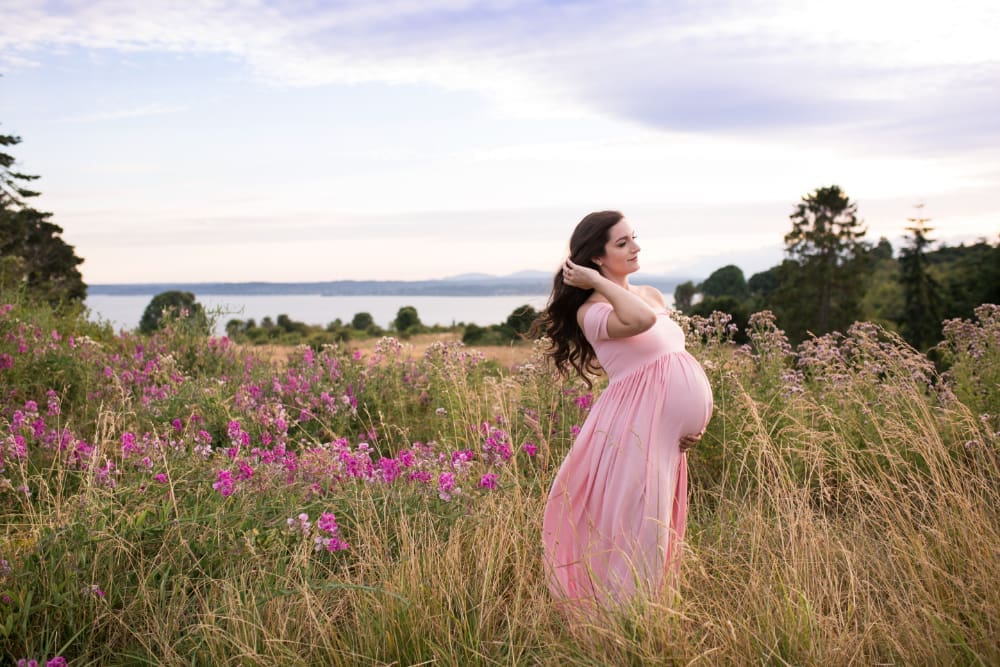 Pregnant mother standing in a wildflower field at sunset, offering outdoor maternity photo ideas.