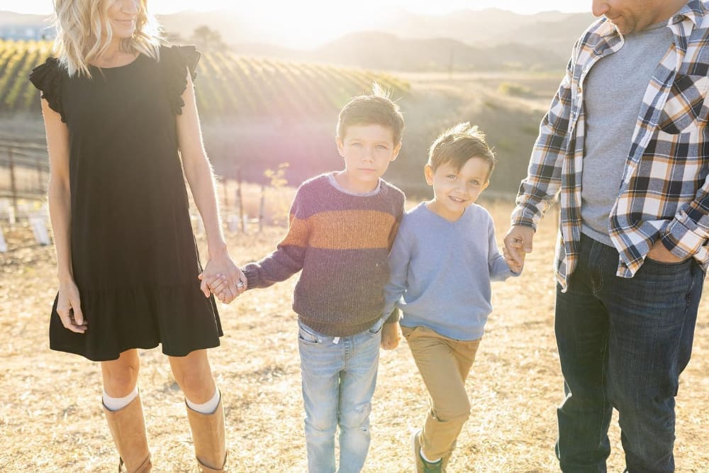 Family walking through a vineyard during golden hour photography, with two young boys holding hands.