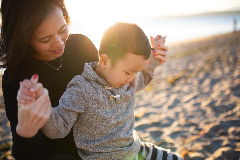 Mother holding her young son’s hands on the beach during a warm golden hour photography session.