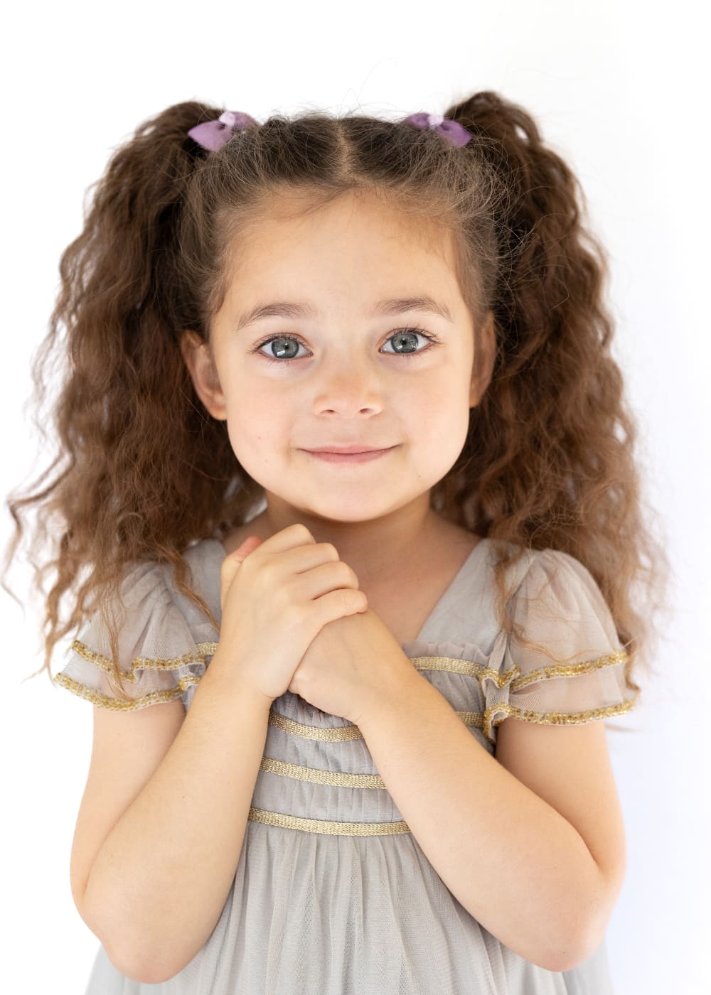 Smiling young girl with curly hair photographed on a white background for preschool picture day.