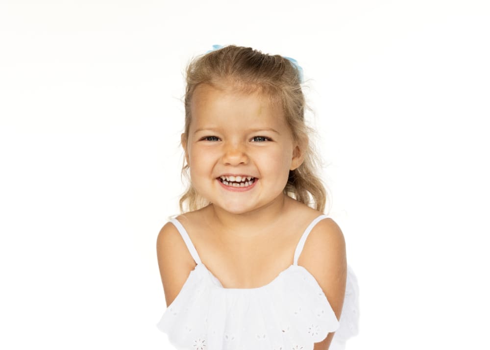 Laughing young girl with pigtails posing for a portrait against a simple white background.