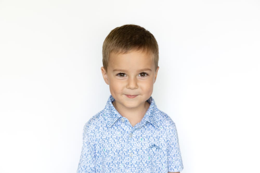 Young boy smiling softly against a simple white background during his preschool picture day portrait.