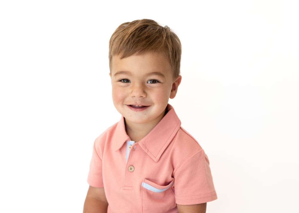 Smiling young boy in a pink collared shirt photographed against a clean white background.