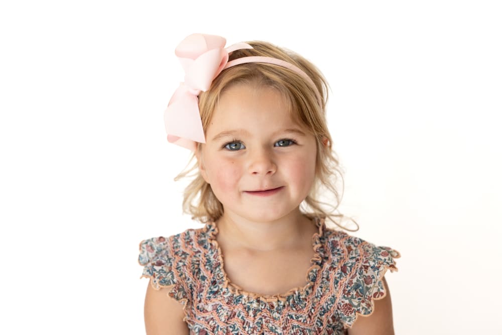 Smiling young girl in a floral dress posing against a white background for preschool picture day.